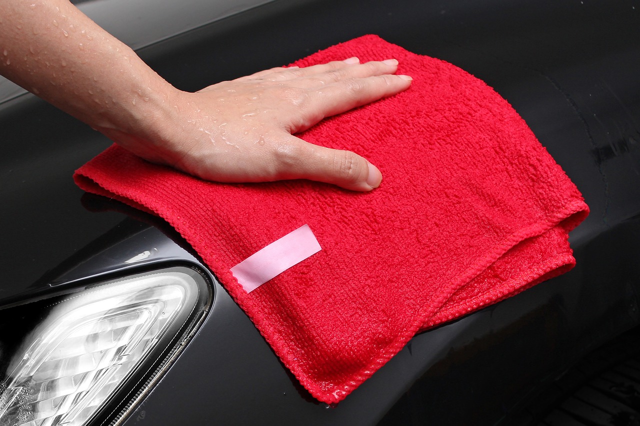Person touching a red microfiber cloth on a car