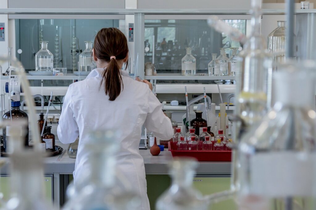 Person wearing a white lab coat, back to the camera, working in a lab