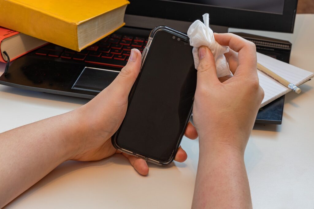 Person wiping down the top of a cell phone with a cloth or paper towel
