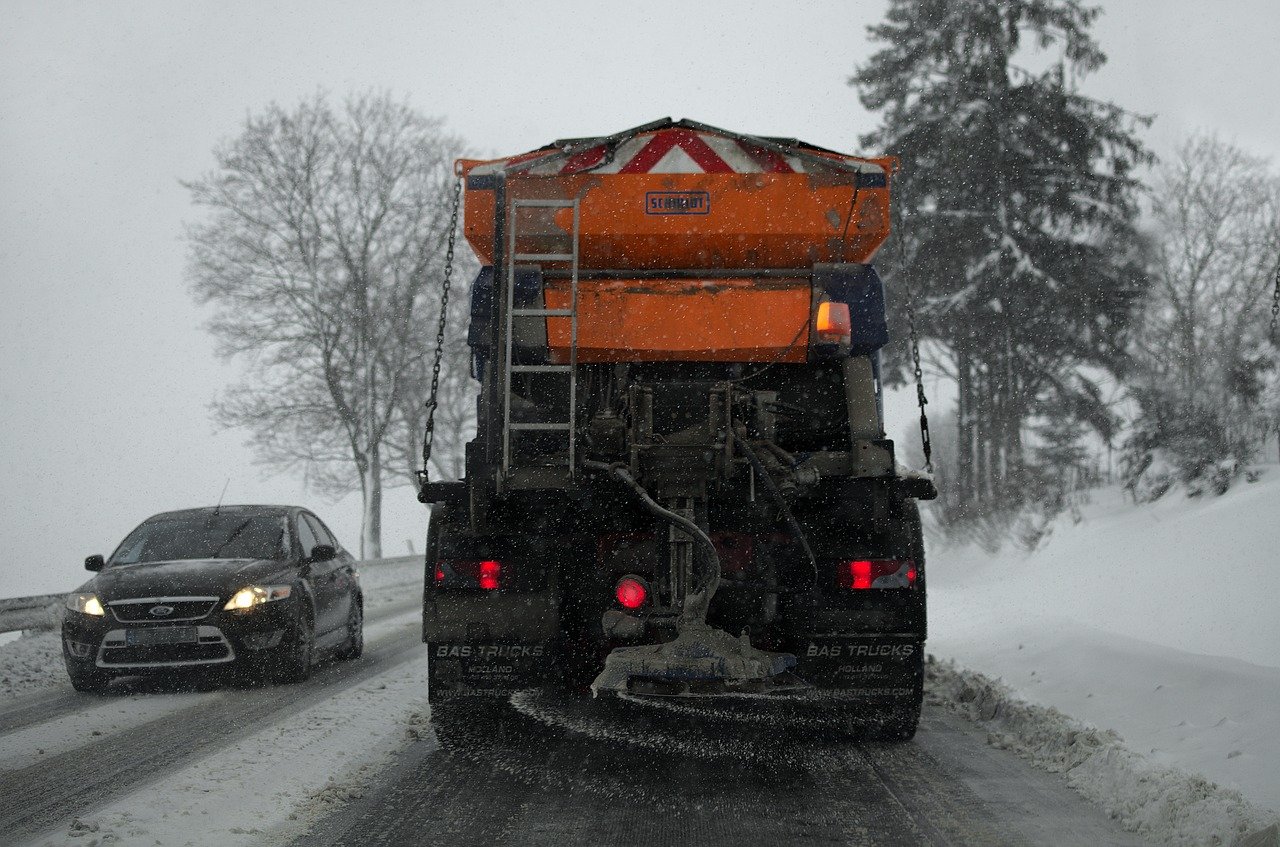 The back side of a snow plow spreading salt and sand on the road