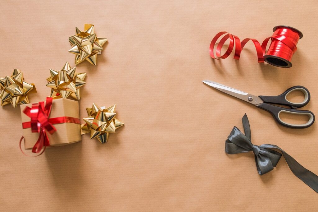 Presents, bows, ribbon, and scissors sitting atop brown paper.